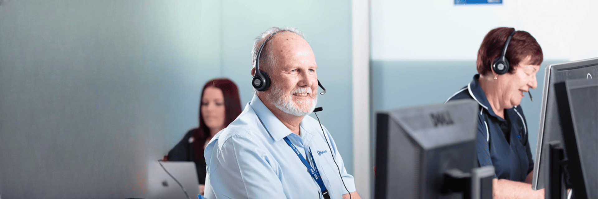 Man in call centre wearing headset smiling at computer screen