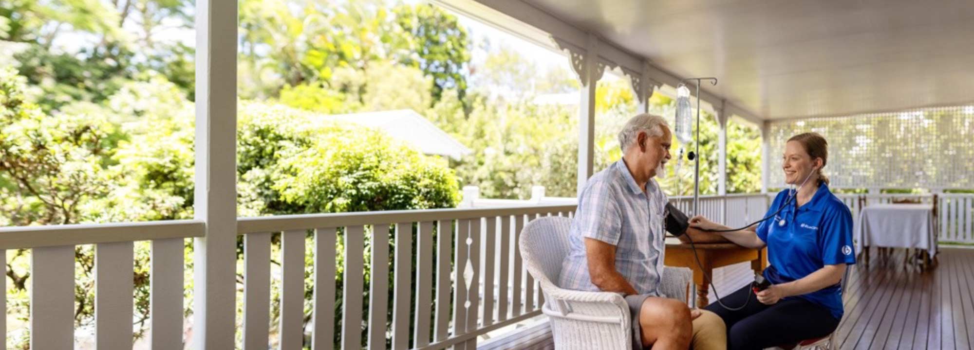 A BlueCare nurse checks the blood pressure of a patient as they sit on his verandah overlooking leafy gardens.