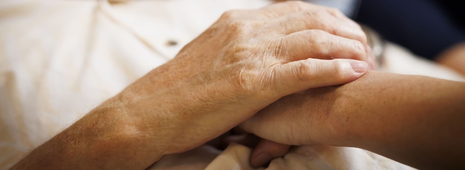A close up photos of a Blue Care employee holding the hand of an older man