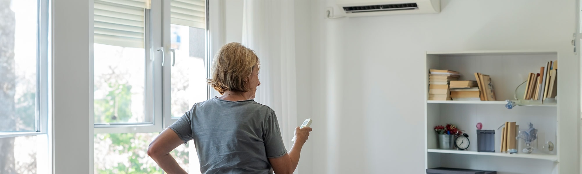 A lady standing in a living room pointing a remote control at an airconditioner