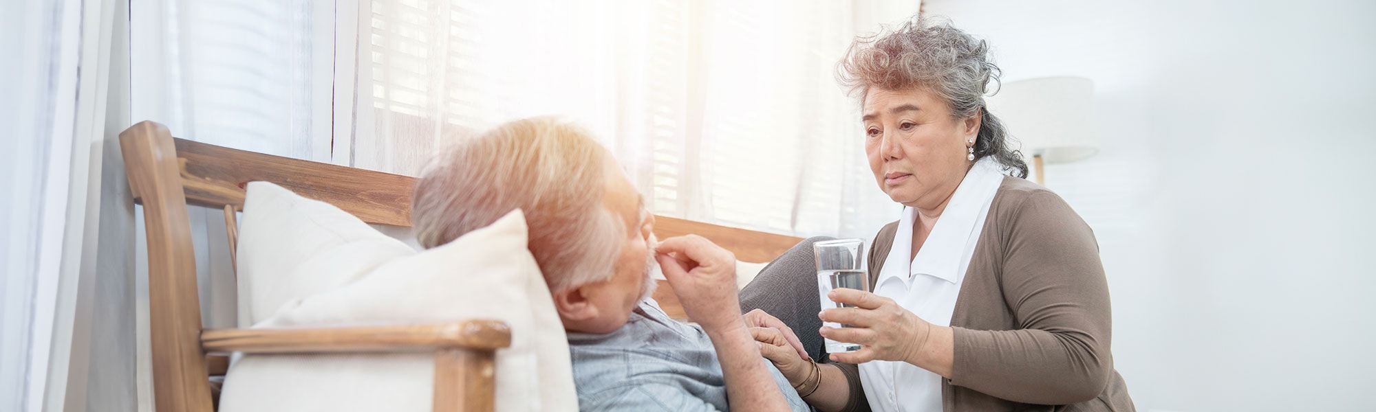 An lady holding a cup of water for an elderly man lying on a couch about to swallow a tablet