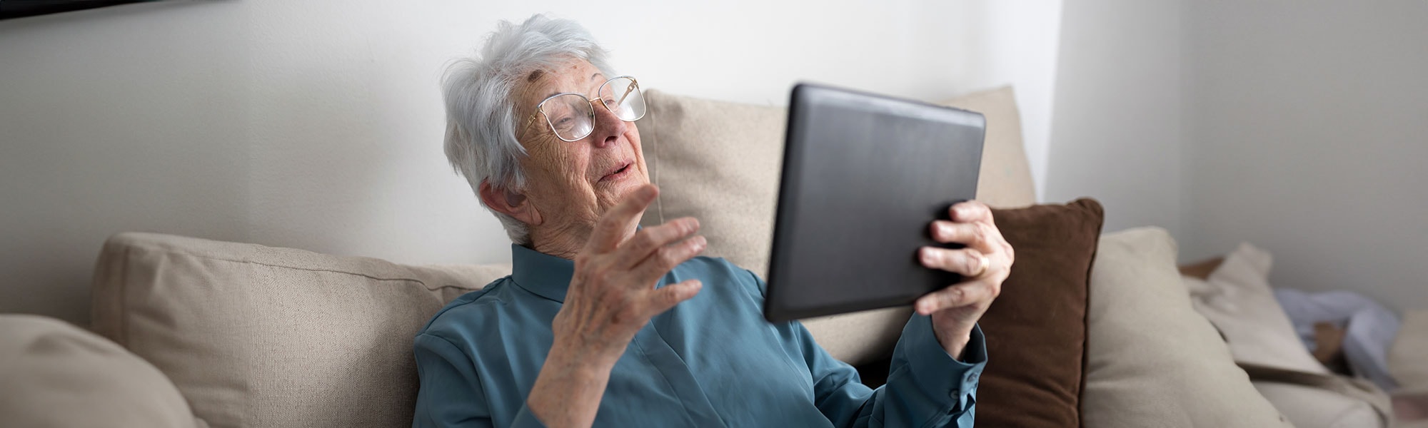An elderly lady sitting on a couch viewing an iPad
