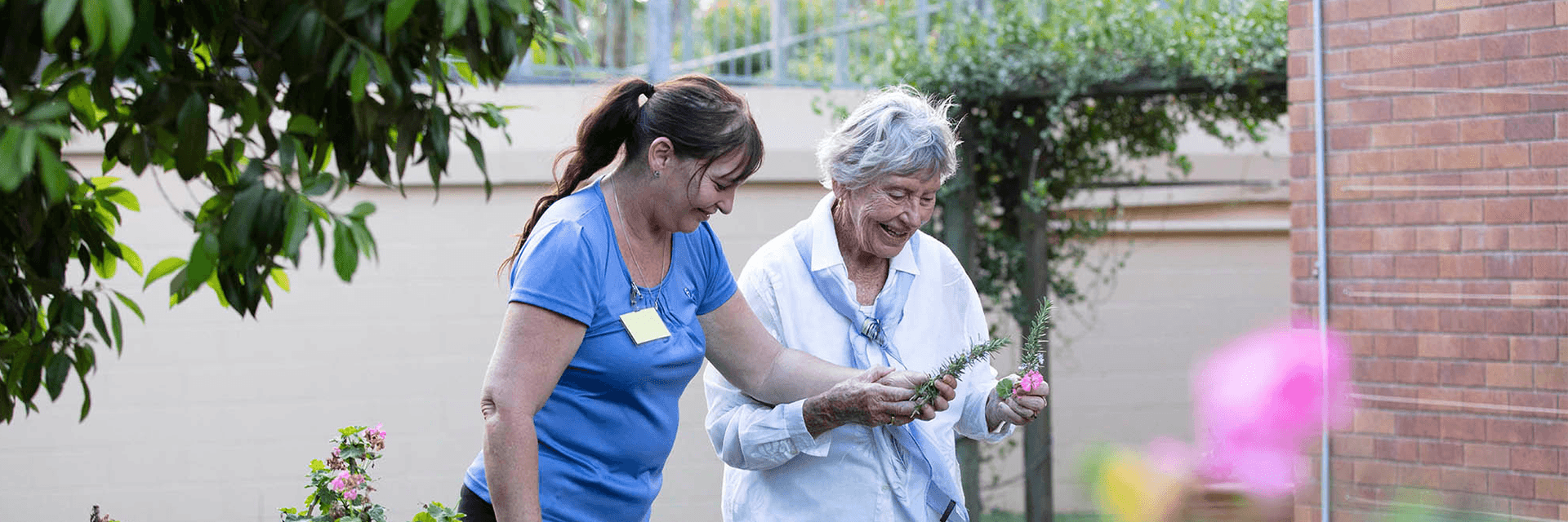 A Blue Care employee supports an older lading living with dementia to work in her garden.