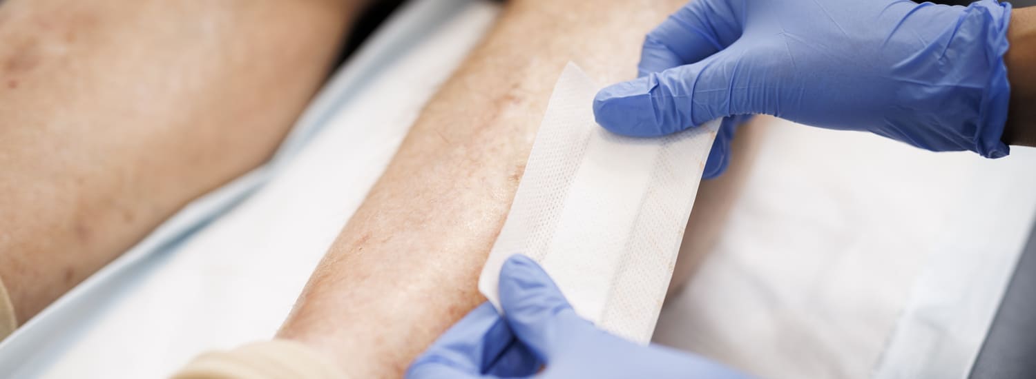 A BlueCare nurse attends to an older man's leg wound dressing