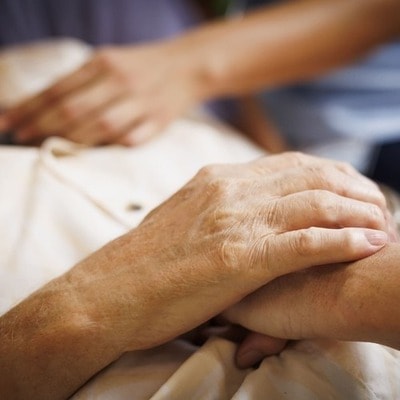 A close up photos of a Blue Care employee holding the hand of an older man