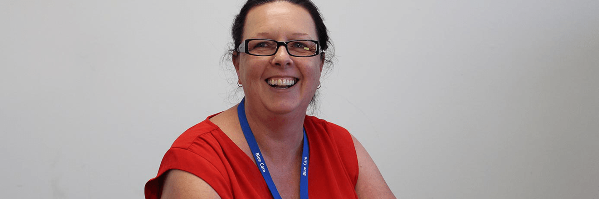 Blue Care home care package specialist Karen Karen is a smiling woman, wearing glasses, a red shirt and a blue Blue Care lanyard.