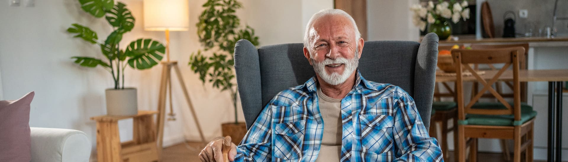 Smiling older man with a white beard sitting in a cosy armchair at home