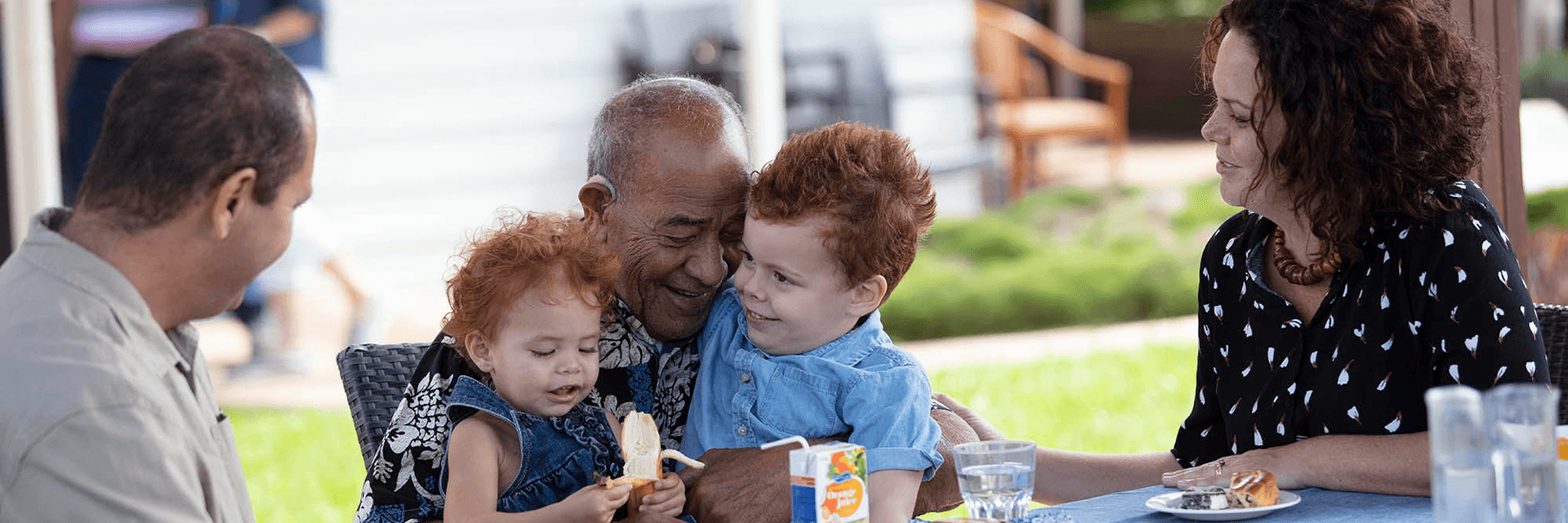 A grandfather, children and grandchildren enjoy eachother's company over lunch outside