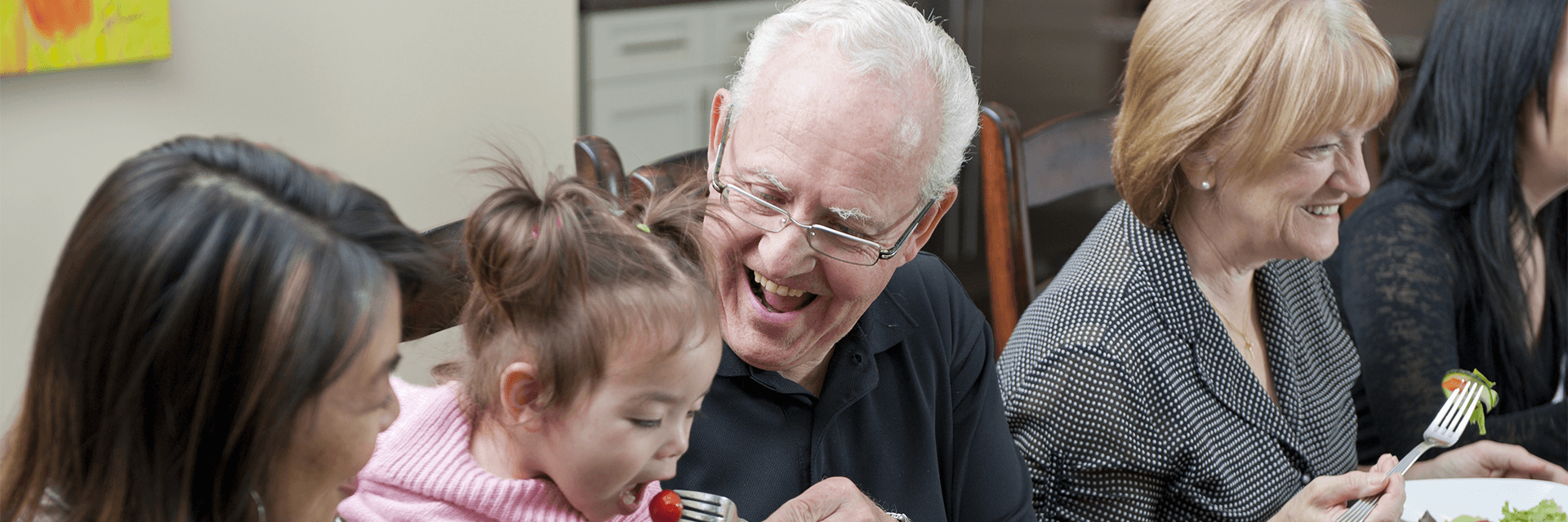 Elderly man at dinner feeding young girl