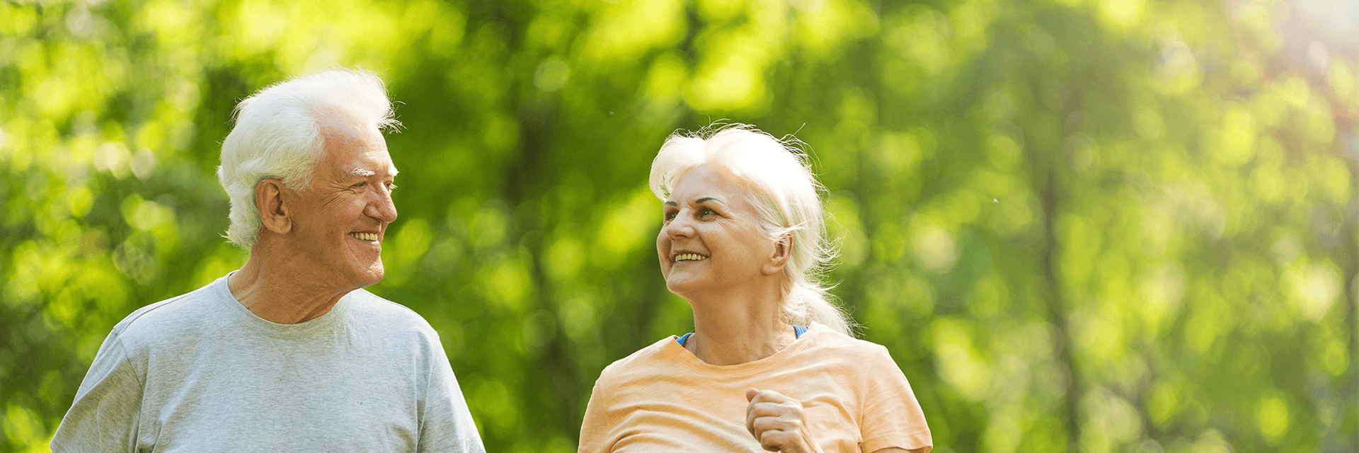 Elderly couple jogging through park and smiling