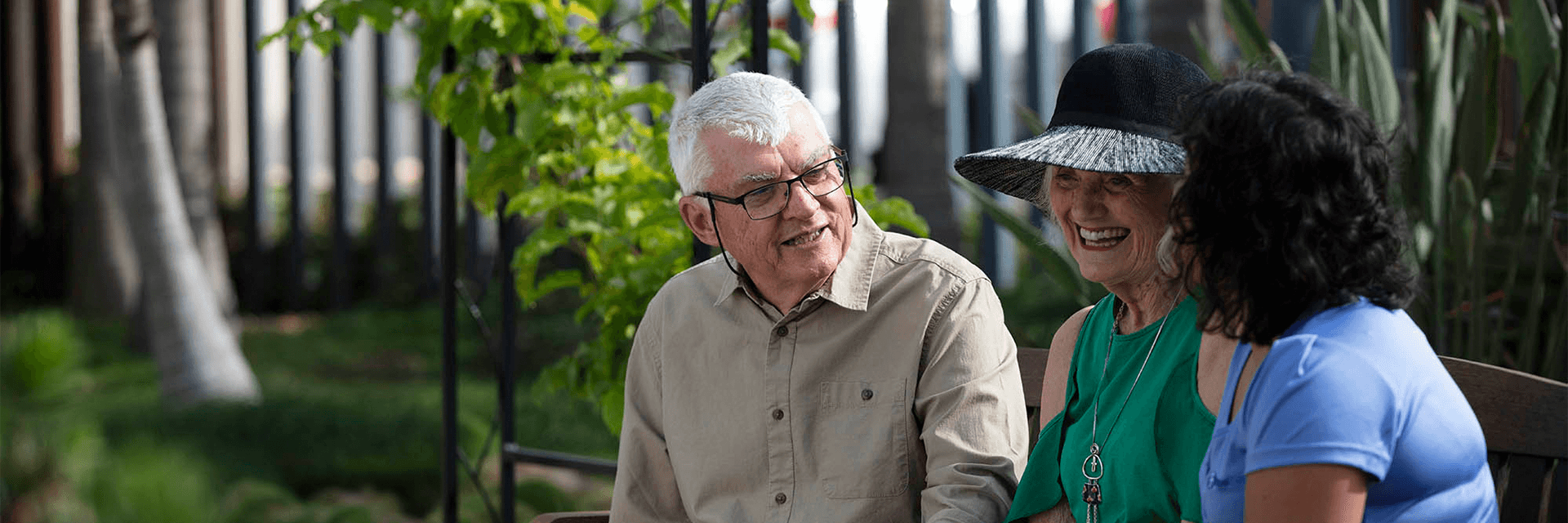 A happy older couple in coversation with a Blue Care employee on a park bench