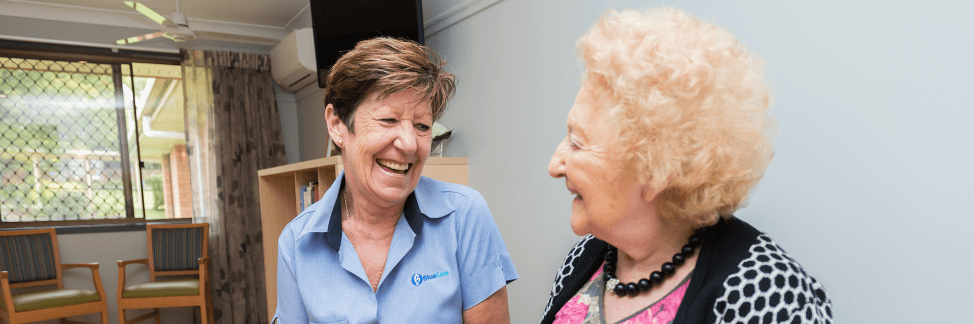 A Blue Care employee smiling at an older lady in her room