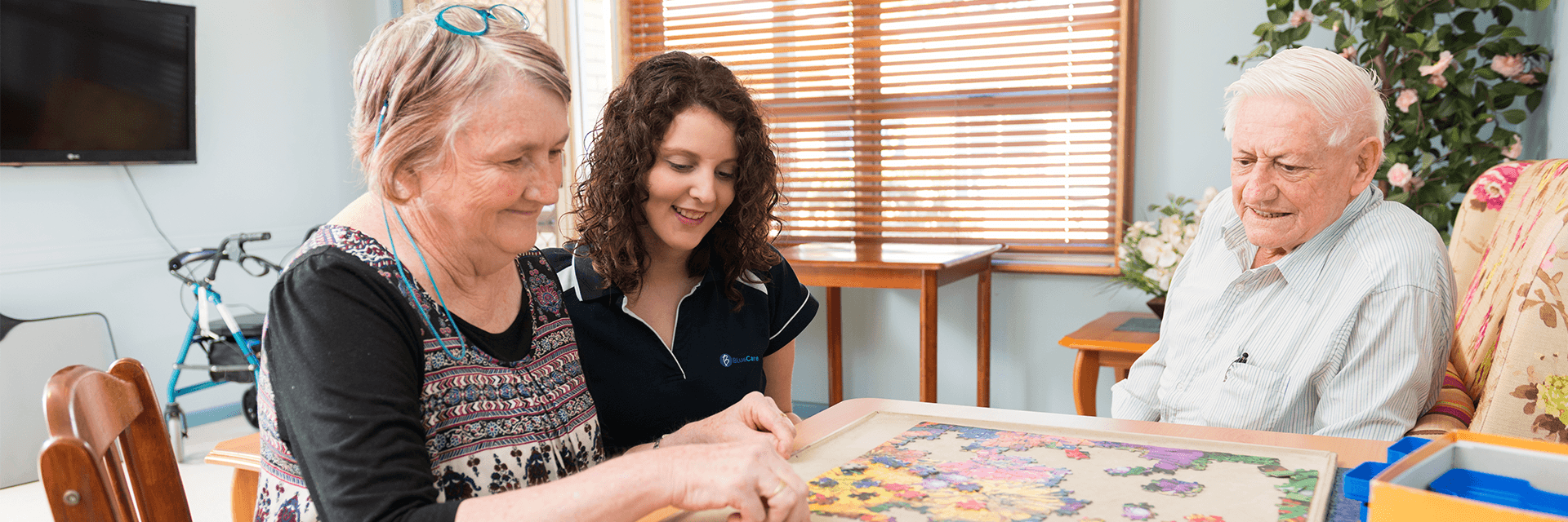Putting the pieces together at Blue Care Brassall Aged Care Facility An older lady, Blue Care worker and an older man work on a jigsaw puzzle in a common area of Blue Care Brassall Aged Care Facility.