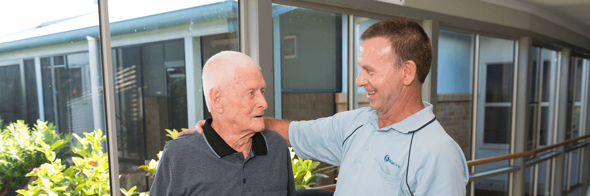 Good mates at Bundaberg Riverlea Aged Care Facility A Blue Care staff member puts his arm around an older gentleman in a common area of Blue Care Bundaberg Riverlea Aged Care Facility.