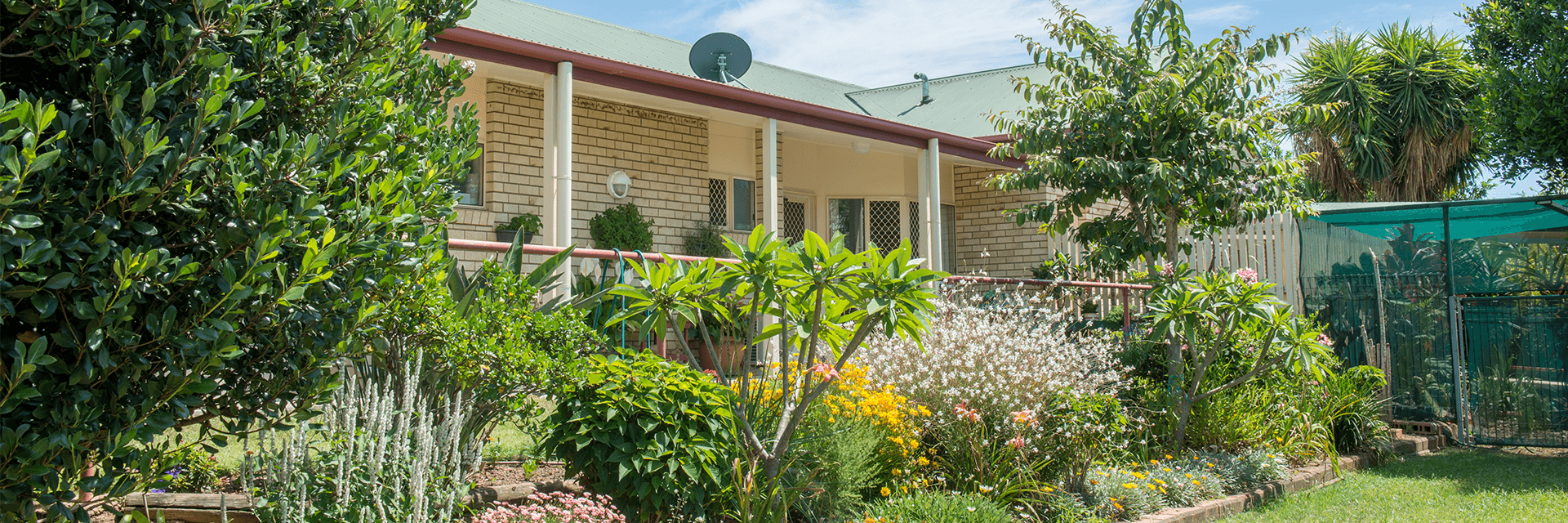Nature's finery at Blue Care Lowood Glenwood Aged Care Facility A glorious garden bed filled with shrubs, frangipani trees, and colourful flowers lines a building at Blue Care Lowood Glenwood Aged Care Facility.