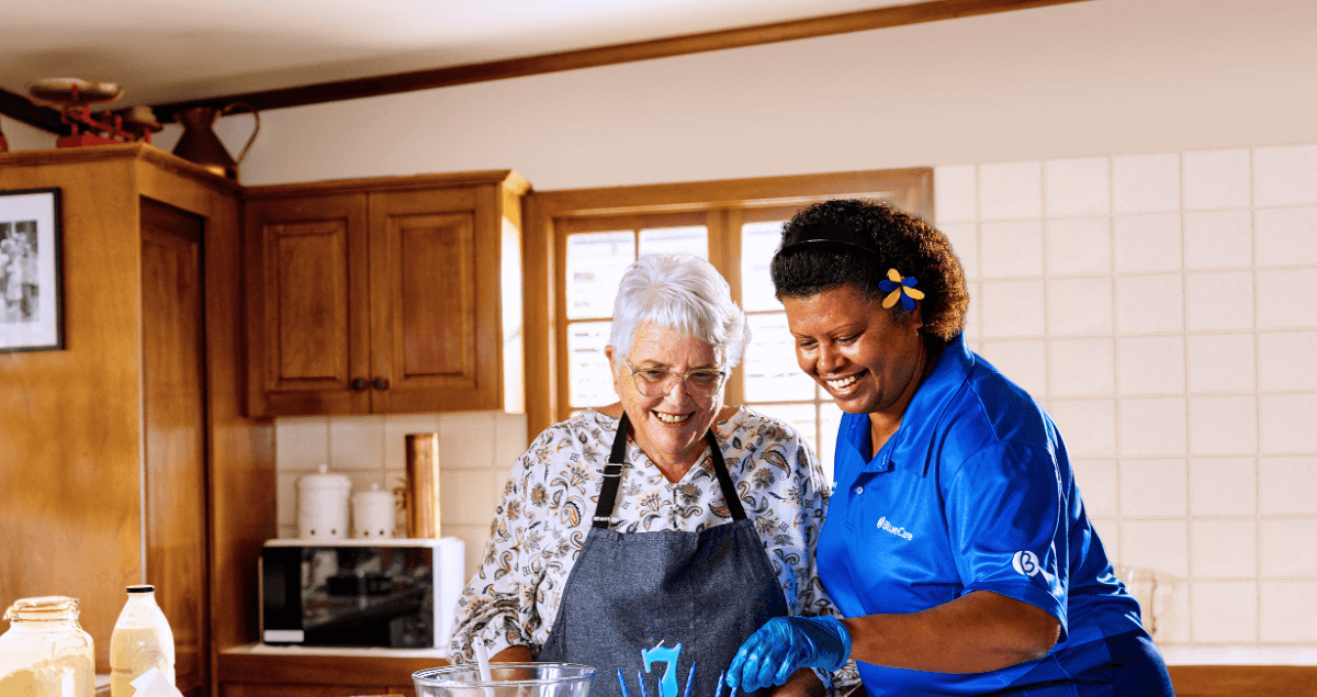 BlueCare employee Bulou Talatoka supports an older lady to make a birthday cake.