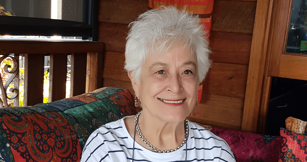 Image alt tags: Lesley Kent sits on a colourful couch on her verandah.