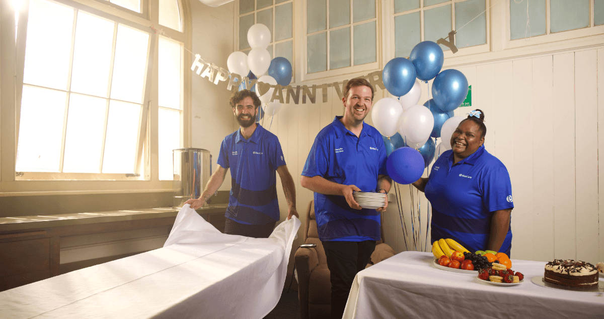 Three BlueCare employees set up tables and balloons for an anniversary party.