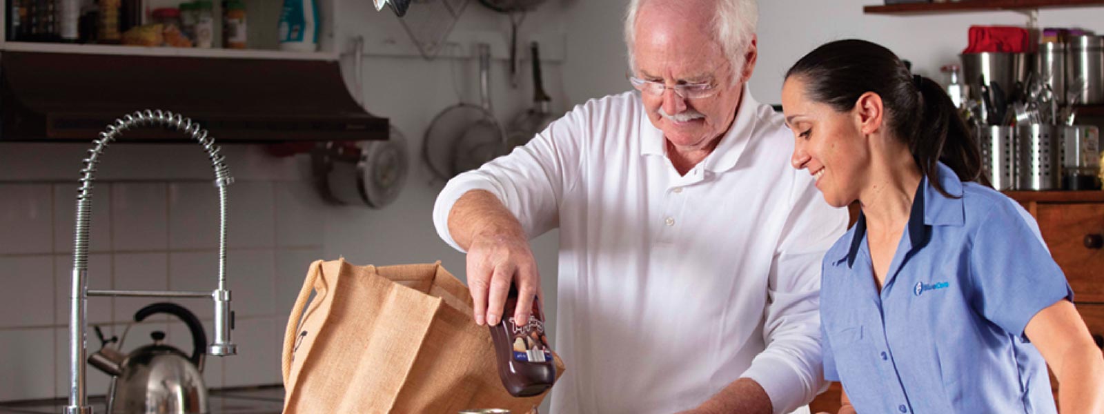 BlueCare staff member helping elderly man take groceries out of a bag in the kitchen