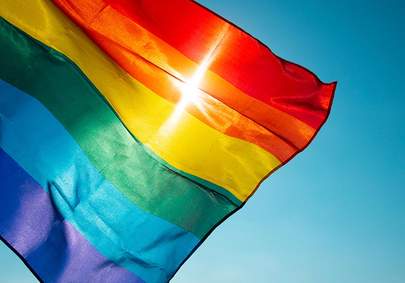 A pride flag waving in front of the sunlight